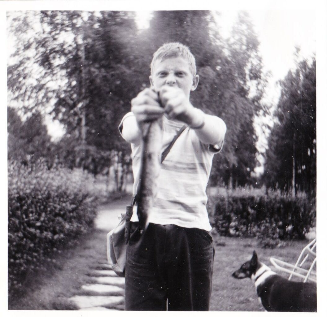 Det är 1963. Bilden är 6*6 så den är tagen med min pappas kamera och troligen av honom själv. Har fått en liten gädda i Klarälven i Munkfors. Liten... tyckte jag inte då. Hunden i bakgrunden var grannens. Den lystrade till namnet Klinga. Fiskevässkan som jag hade skickat efter. T-shirten som jag hade fått av min pappas kusin i USA. 